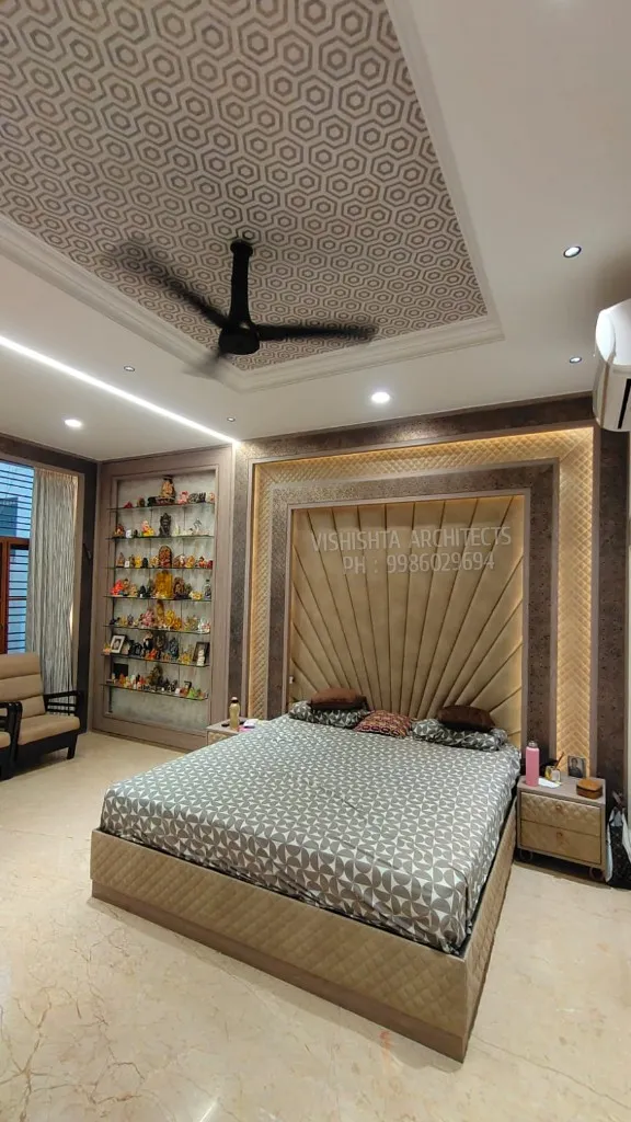 Bedroom with a radial channel-tufted gold fabric headboard wall bordered by textured wallpaper, a hexagon-patterned printed ceiling