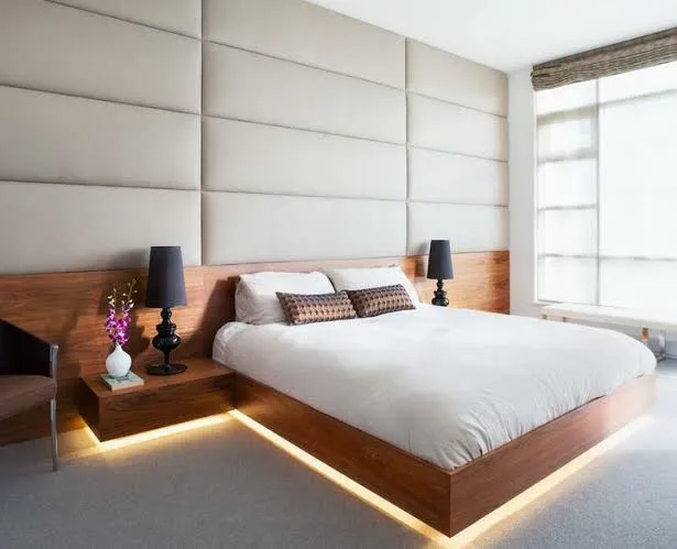 Bedroom with a walnut platform bed featuring built-in under-bed LED lighting and integrated floating nightstands, set against a cream upholstered panel wall.