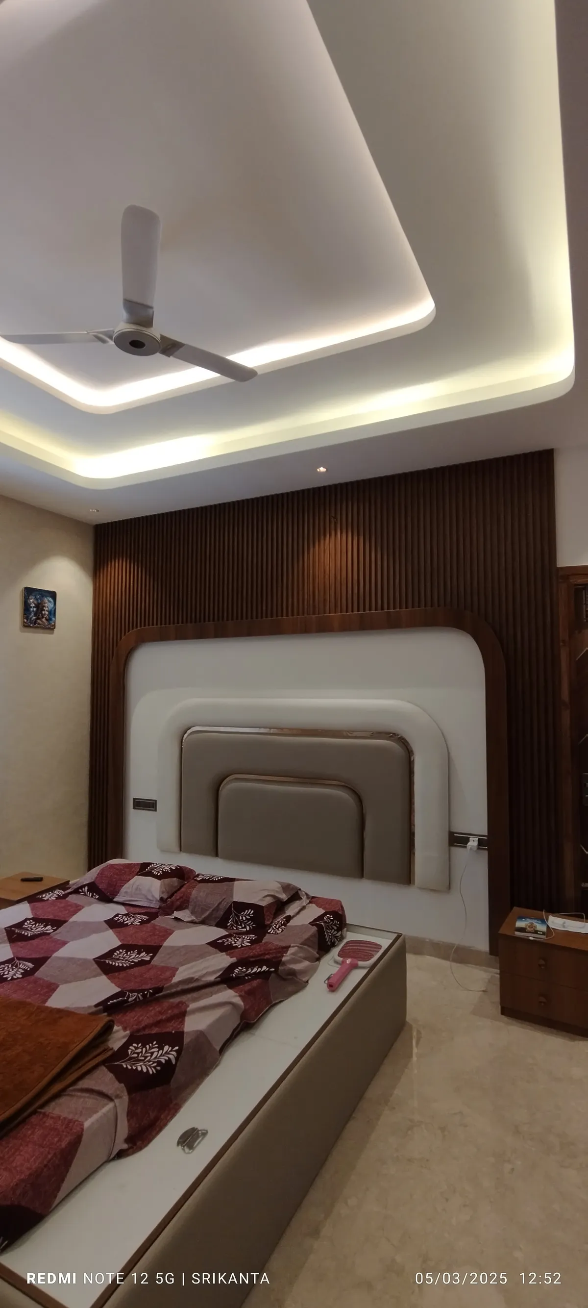 Phone snapshot of a bedroom where three stepped rounded-corner upholstered headboard frames are set into a full-height fluted teak wall