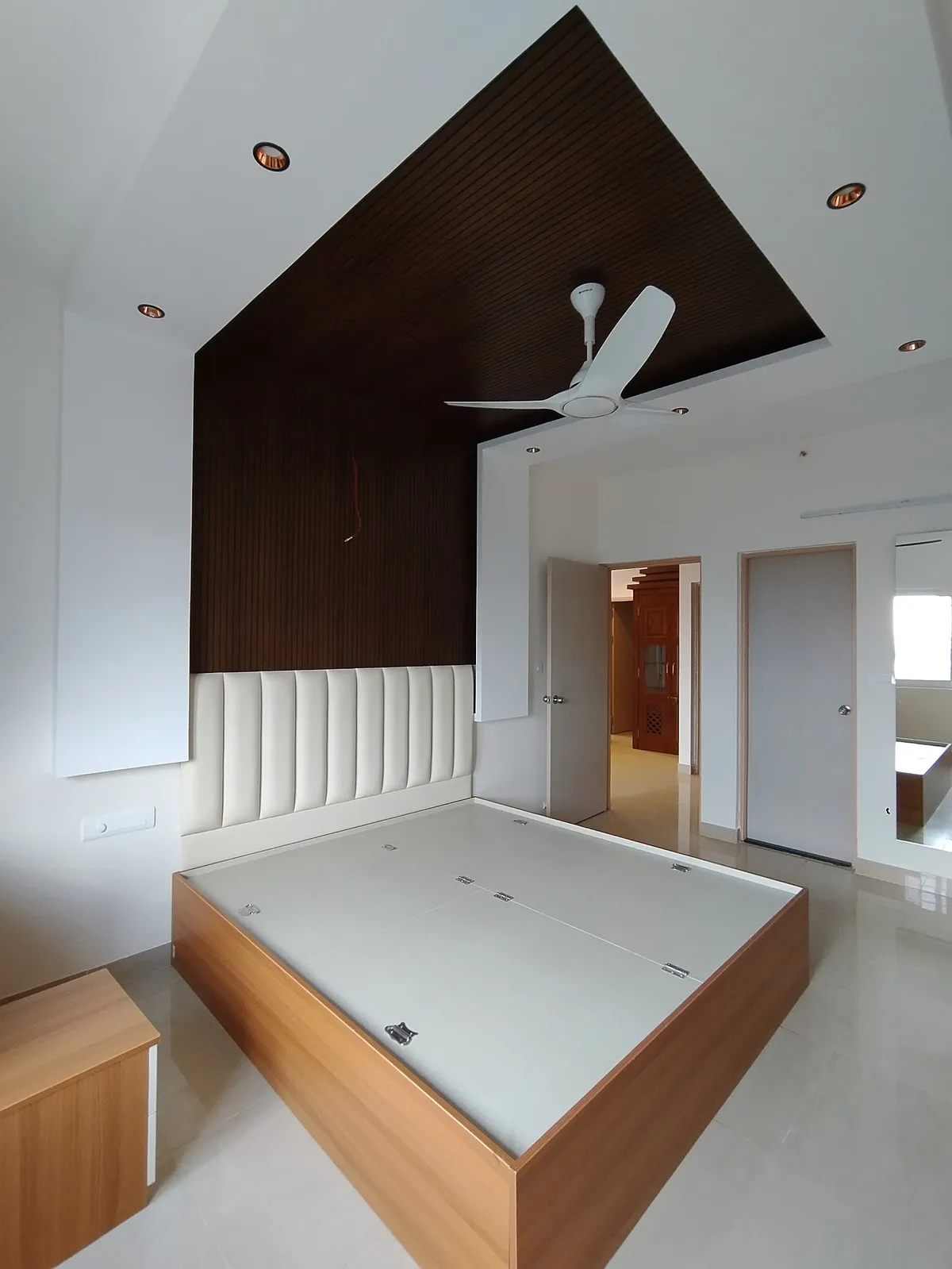 Bare handover shot of a bedroom where a dark fluted panel climbs the headboard wall and folds across the ceiling as one plane