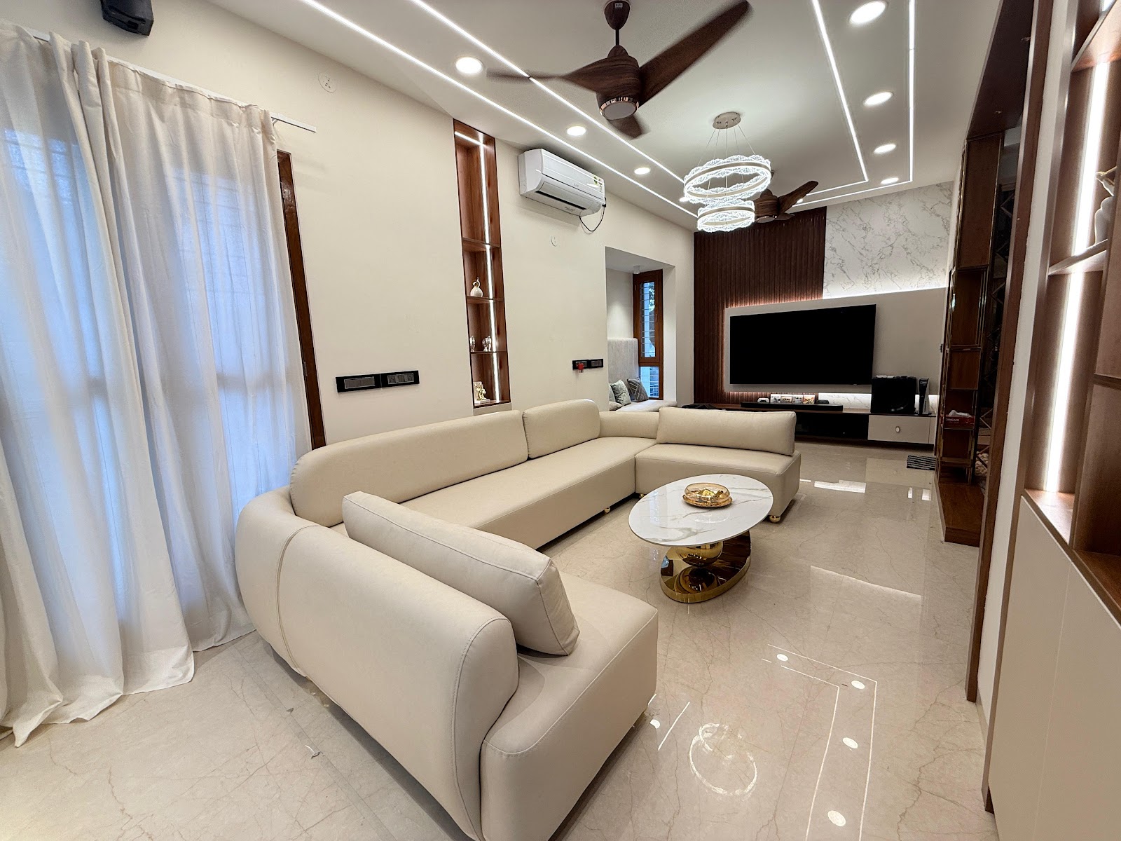 Living room with a large cream sectional sofa, a marble and gold coffee table, and a TV feature wall in marble cladding and wood fluted panelling beneath a