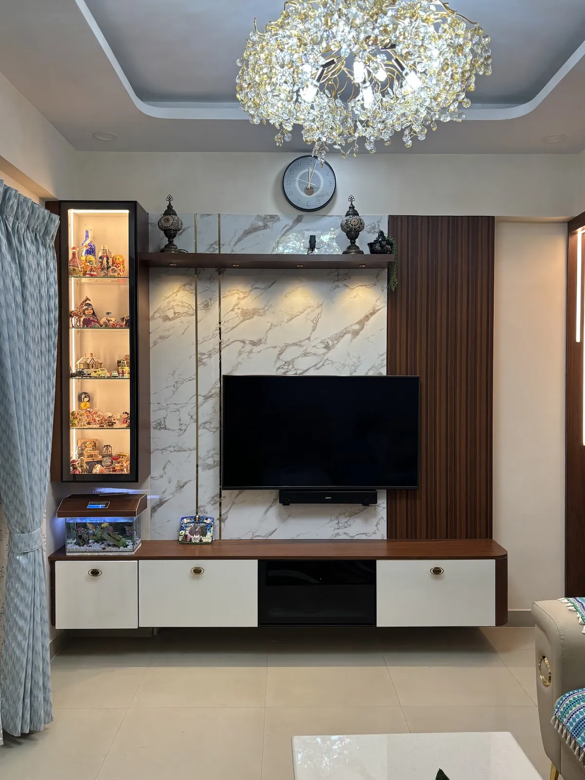 Living-room TV wall in white marble-look slab cladding with thin brass inlay strips, a fluted walnut panel to the right