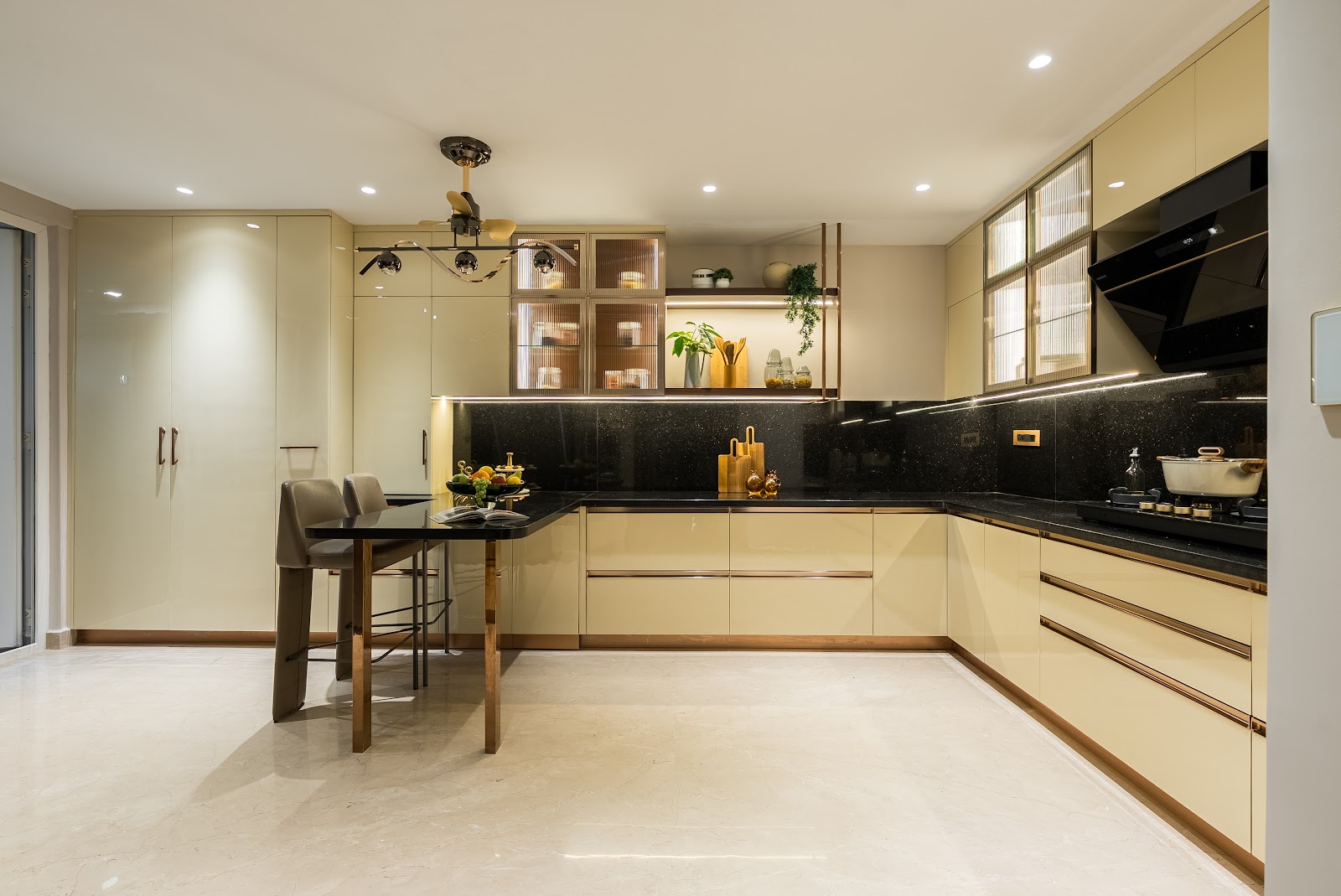 A champagne-and-copper glossy kitchen with a black speckled-stone counter and backsplash, glass-front upper cabinets, a chimney hood