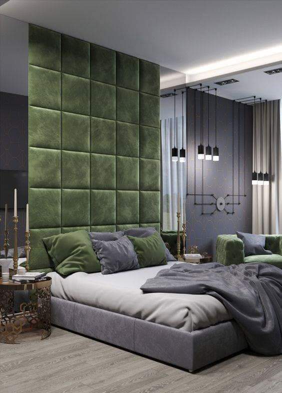 Render of a bedroom with a floor-to-ceiling emerald tufted-velvet headboard wall, a cluster of bare-bulb pendant lights and a dark geometric-patterned accent