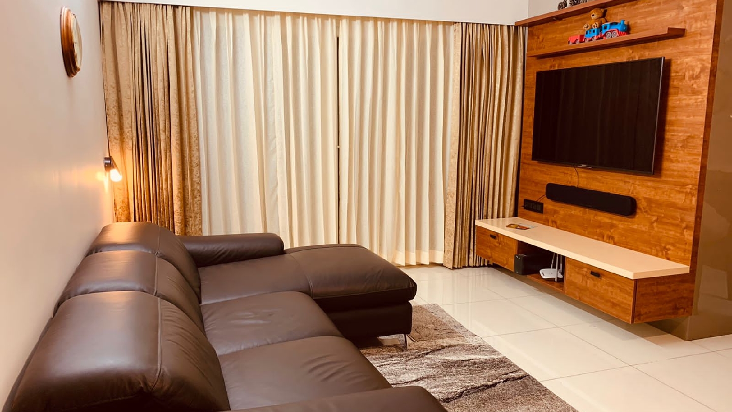 Living room with a dark brown leather L-shaped sofa facing a wood-panelled TV wall with a floating console, floor-length curtains and a patterned area rug.
