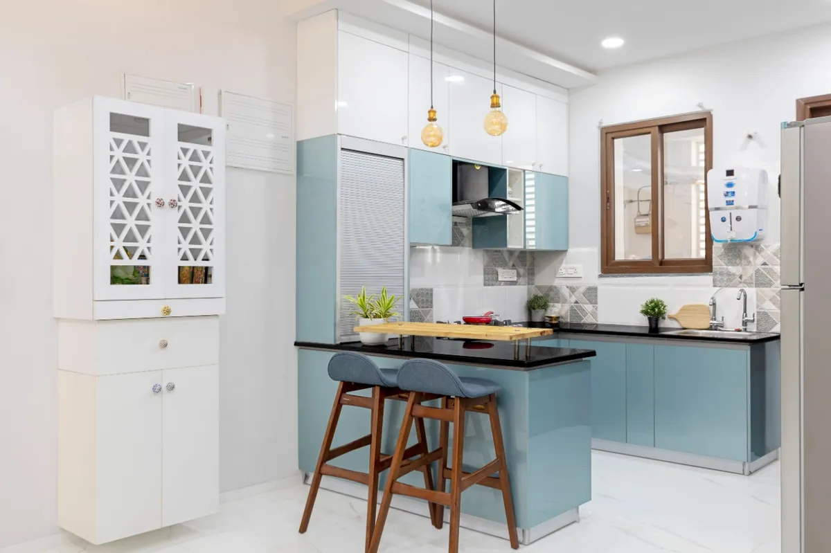 Powder-blue high-gloss kitchen with a peninsula breakfast counter and two wooden bar stools, Edison pendants over the black granite top