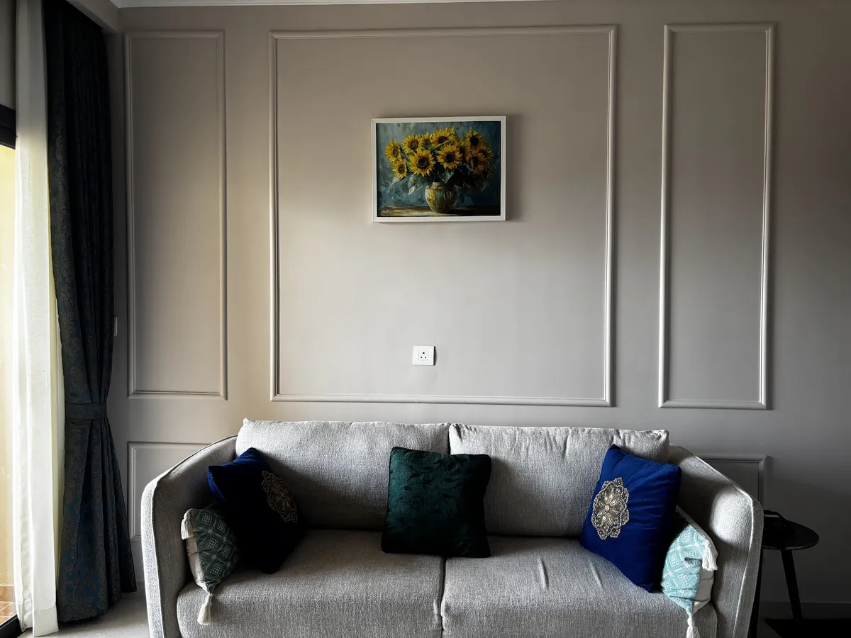 Living room with a wainscot-style panel moulding wall, a framed sunflower still-life painting, and a grey sofa styled with navy