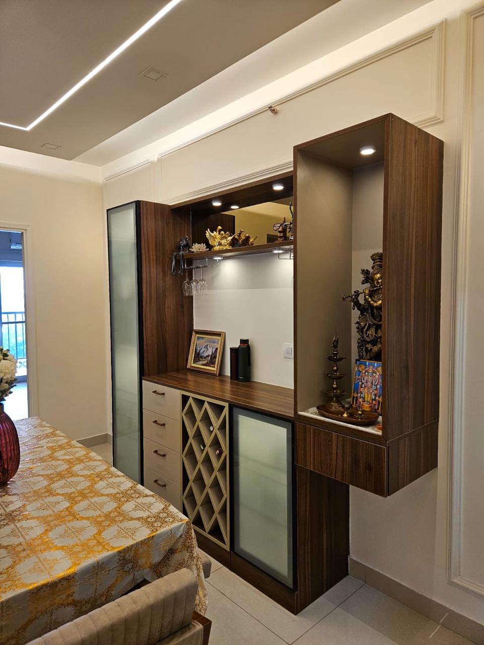 Dining nook with a combined walnut-finish bar and pooja display unit — a wine-glass rack and frosted-glass bar cabinet on the left