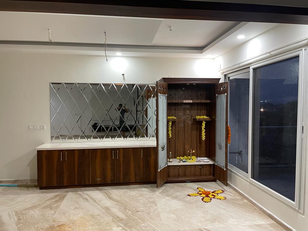 Pooja cabinet with carved wood crown and glass doors open to reveal marigold garlands and a lit oil lamp