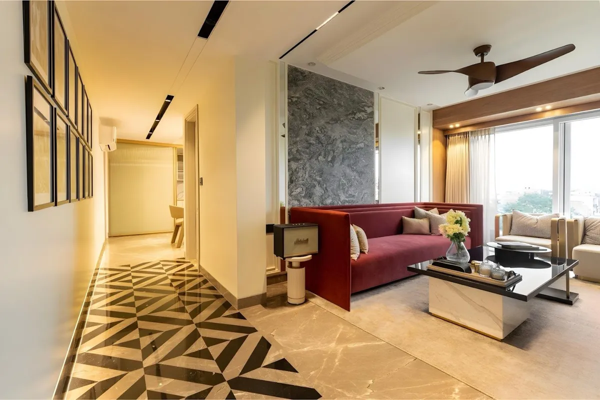 Deep-red velvet sofa set against a grey marble slab wall, with a black-and-cream geometric marble inlay running away down the passage and a grid of
