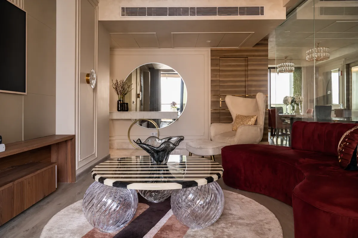 Wine-red curved velvet sofa facing a striped-stone round coffee table carried on three cut-glass sphere legs