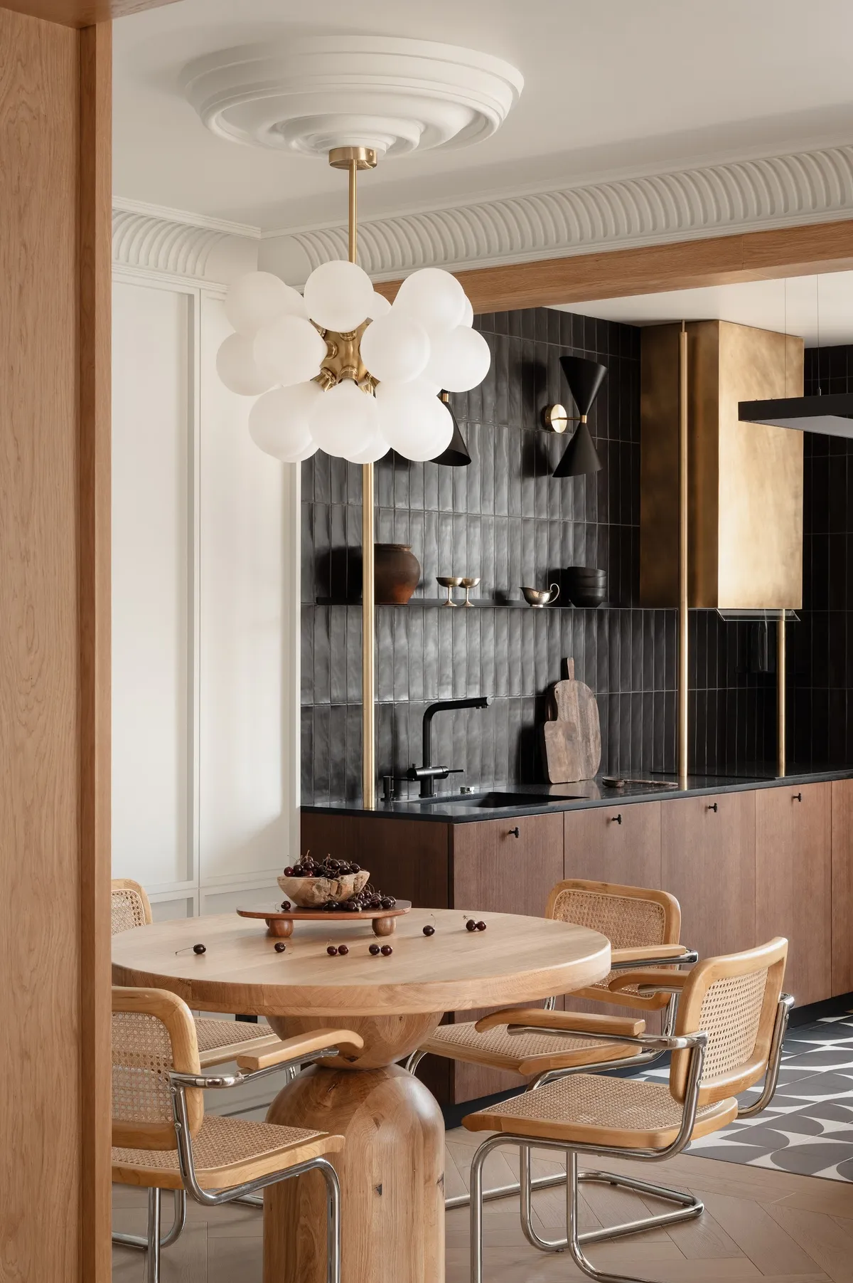 Dining nook with a round oak pedestal table, cane-and-chrome cantilever chairs, and a brass bubble-cluster pendant light