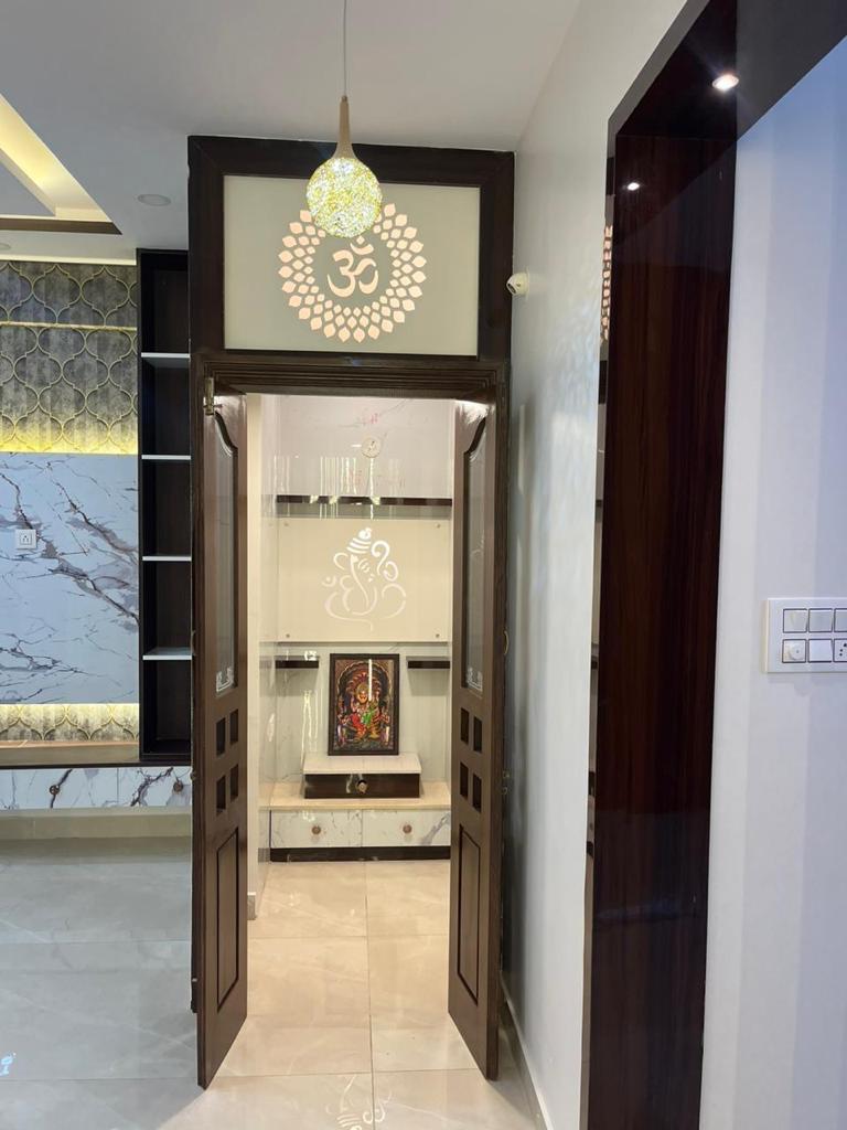 Pooja room framed by a dark wood double door with a backlit Om motif, opening to a white marble unit with a deity silhouette panel.