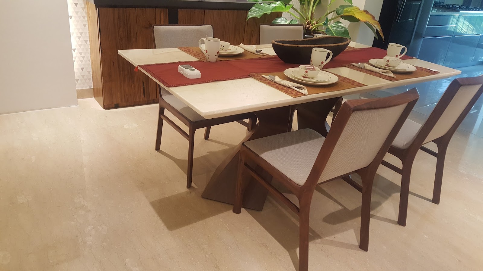 Dining table with a rectangular marble top on a sculptural wood base, styled with a red table runner and place settings for four.