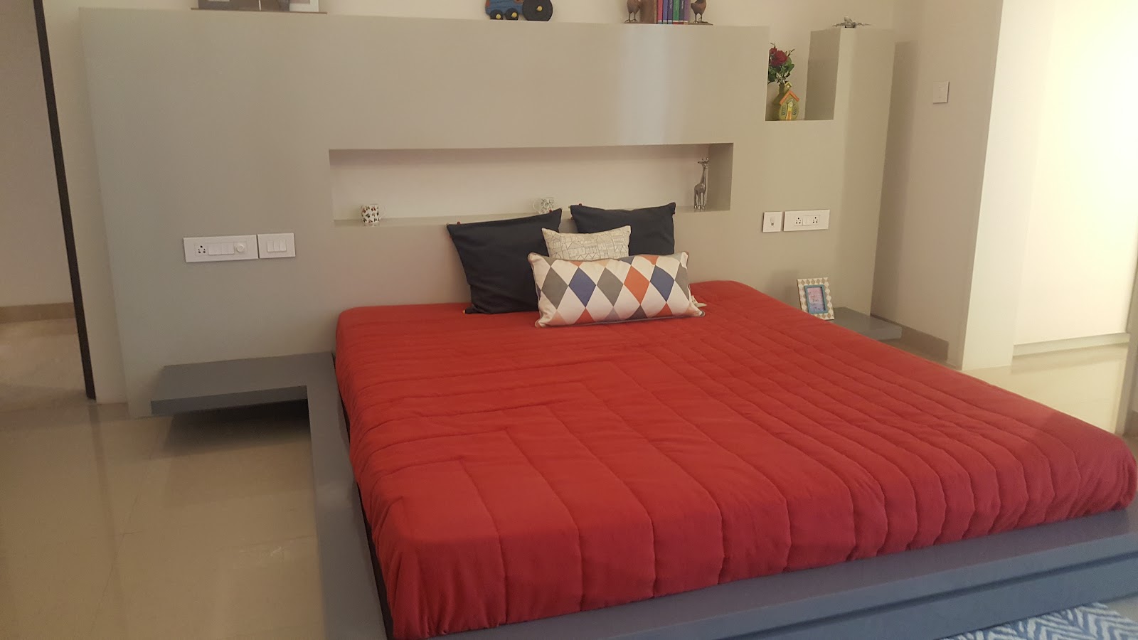 Bedroom with a floating grey platform bed and an integrated headboard wall of display niches