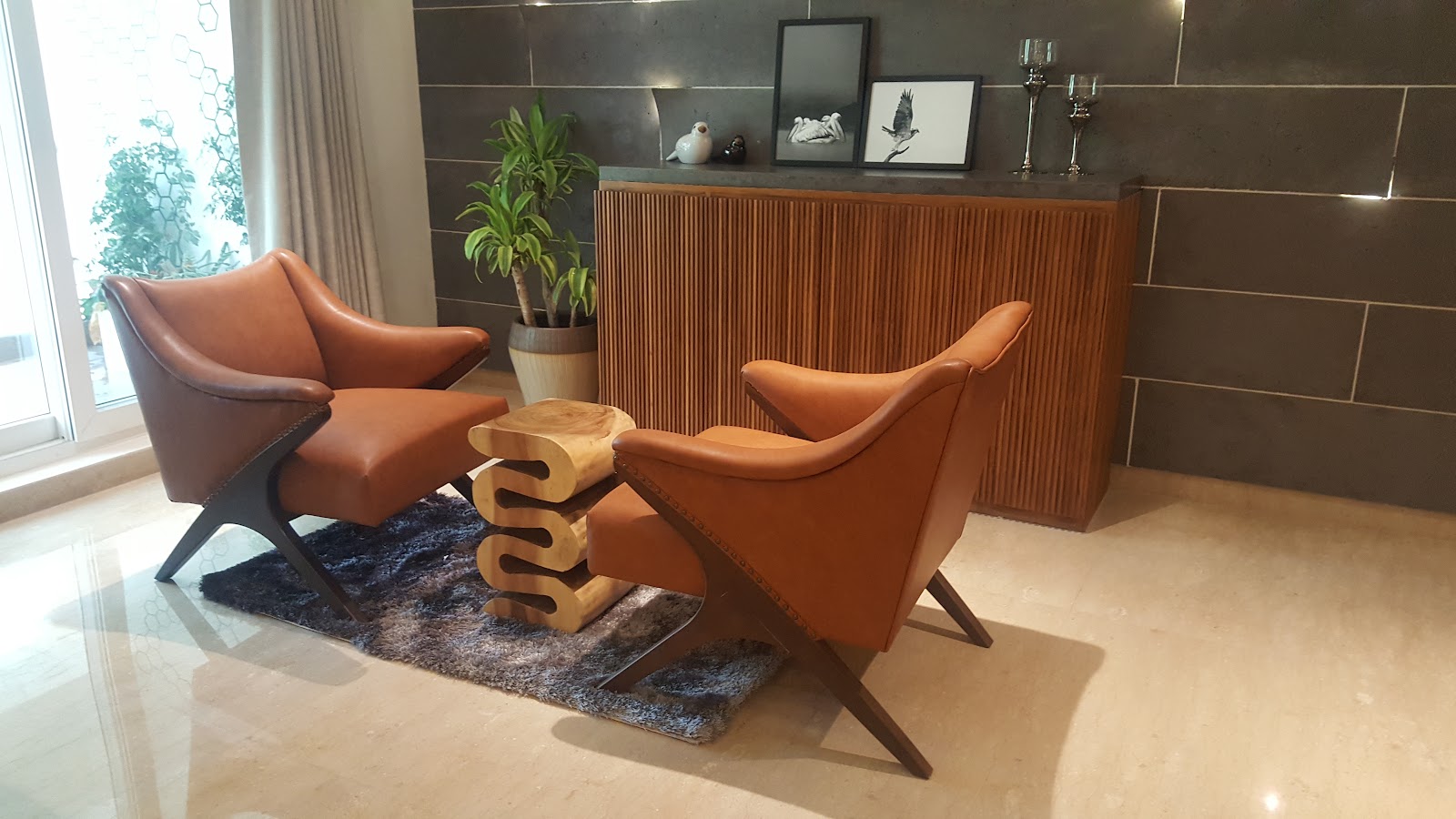 Living room seating nook with two tan leather mid-century armchairs around a sculptural wood stool table