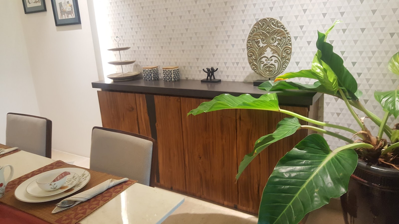 Dining room console styled with ceramic jars, a cake stand and metal sculptures against triangle-patterned wallpaper