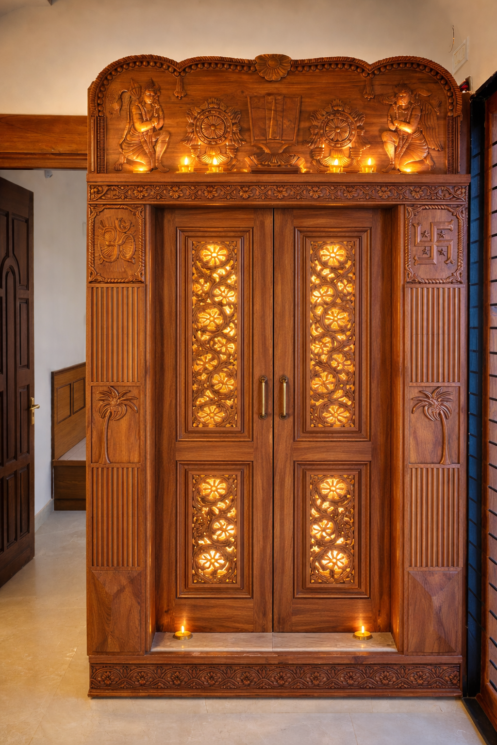 Hand-carved teak pooja mandir doors with backlit floral jaali panels, deity relief work and lit diyas at the threshold.