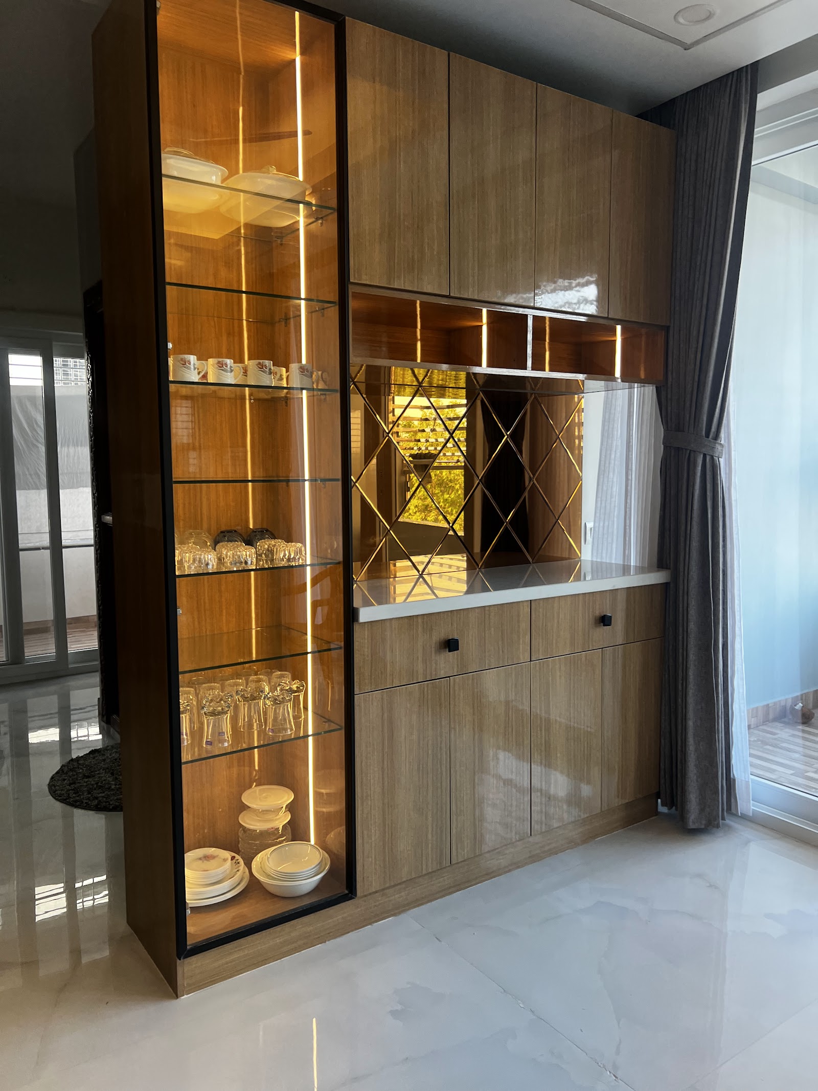 Dining-area crockery and bar unit with a backlit glass display cabinet, a diamond-mirror splashback, and glossy wood-veneer cabinetry topped with white marble.