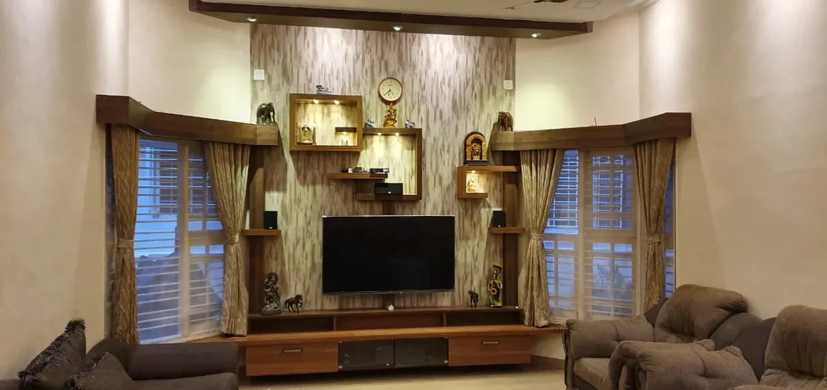 Living room TV unit flanked by curtained bay windows, with a textured wallpaper backdrop and illuminated wood display niches showcasing curios and a wall clock.