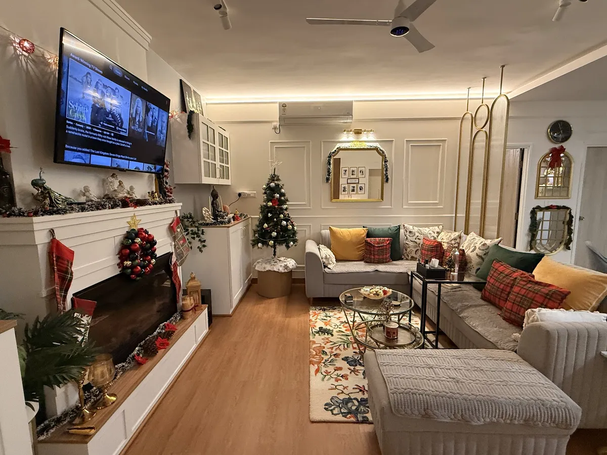Living room with a white panel-moulded wall, mantel-style TV console, sectional sofa and a floral area rug on wood-look flooring, decorated for the holidays.