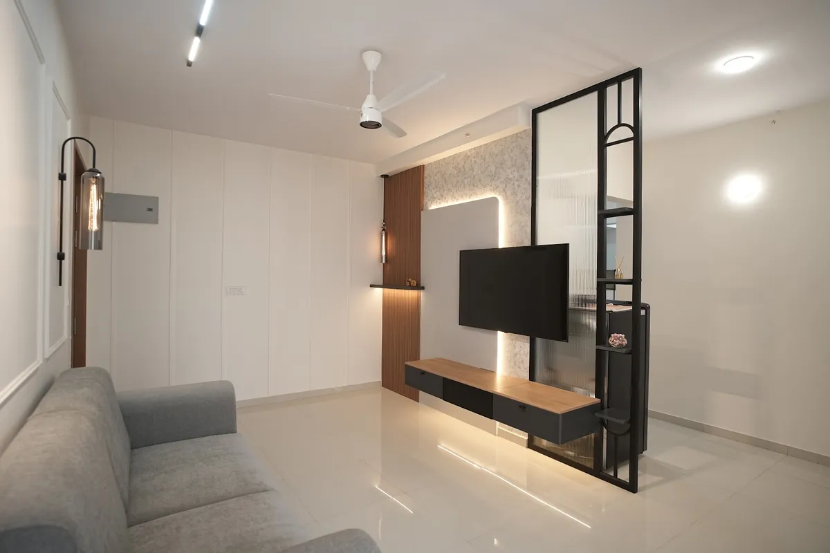Living room with a floating black-and-wood TV console against a backlit floral wallpaper panel, flanked by a black metal-framed fluted glass partition.