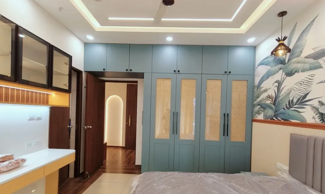 Handover-stage bedroom with a teal wardrobe run inset with cane-mesh panels, a tropical leaf mural beside a fluted grey headboard