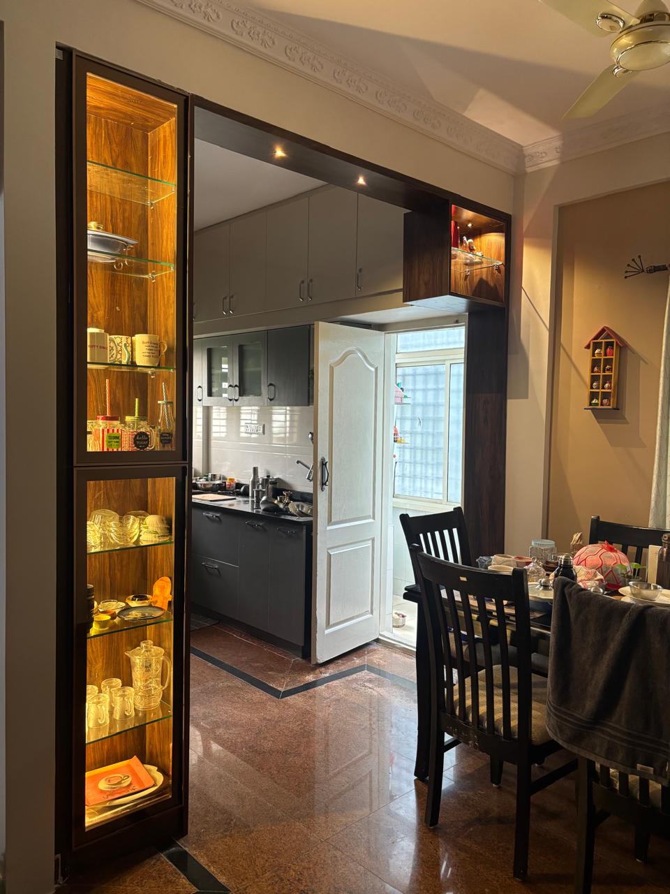 Dining area with a wood-framed backlit glass display cabinet, a dark wood dining table and chairs, decorative ceiling cornice moulding