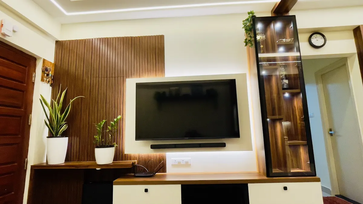 TV wall in a flat's living room: fluted teak-finish panelling to the left of a backlit white recess holding the screen and soundbar