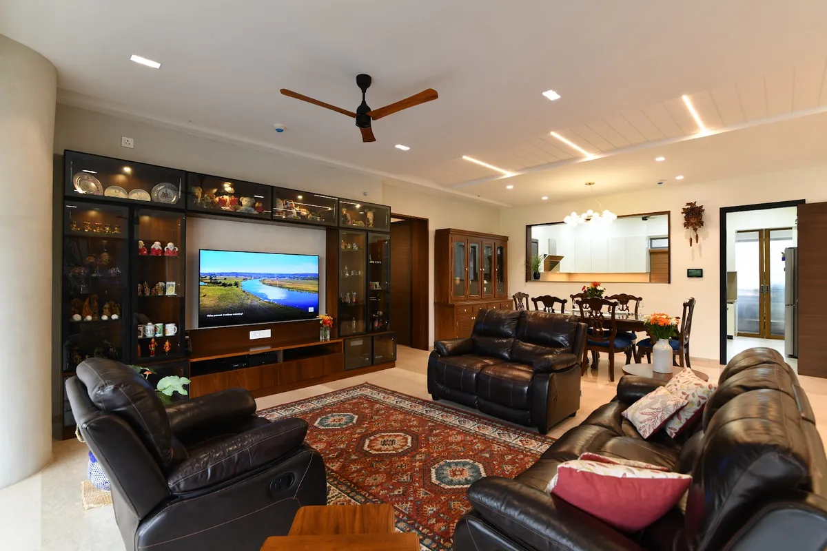 Living room with black leather reclining sofas and a Persian-style rug, a dark-wood TV unit flanked by glass-front display cabinets