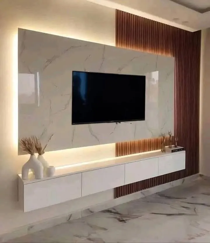 TV feature wall with a backlit book-matched marble panel, a copper-toned fluted wood accent strip, and a floating white lacquer TV console on marble flooring.