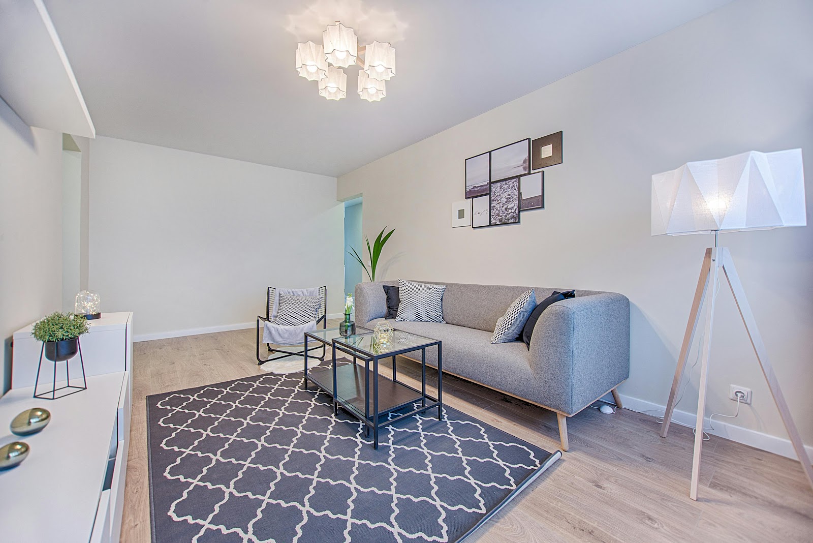 Scandinavian-style living room with a grey woven sofa, a moroccan-trellis rug, glass-and-black-metal coffee table, and a tripod floor lamp.