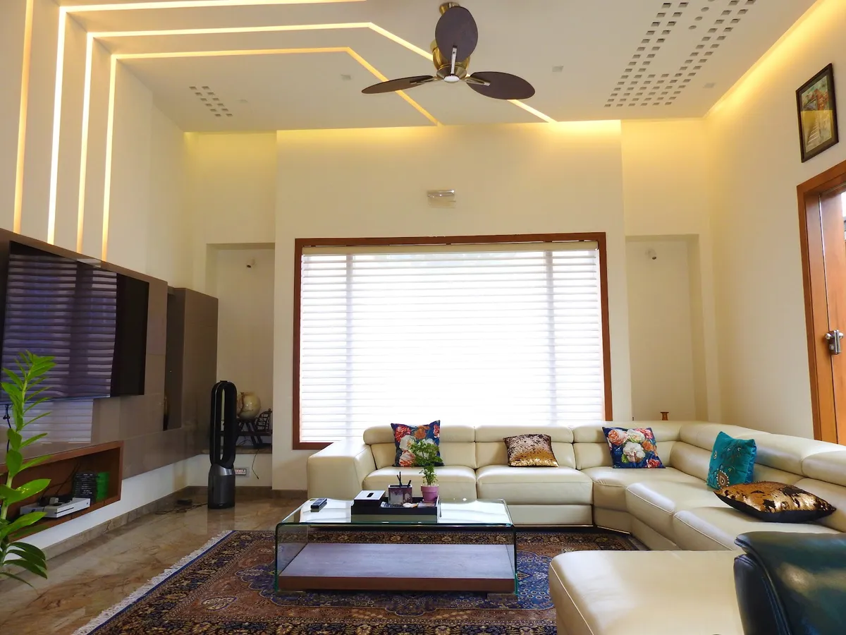 Living room with an angular cove-lit false ceiling, a cream leather sectional sofa with colourful cushions