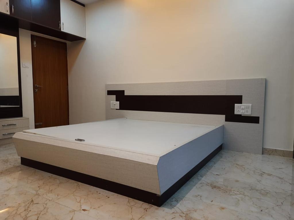 Bedroom with an upholstered platform bed against a wood-veneer wardrobe wall, a fabric-upholstered headboard panel with dark wood accent stripes