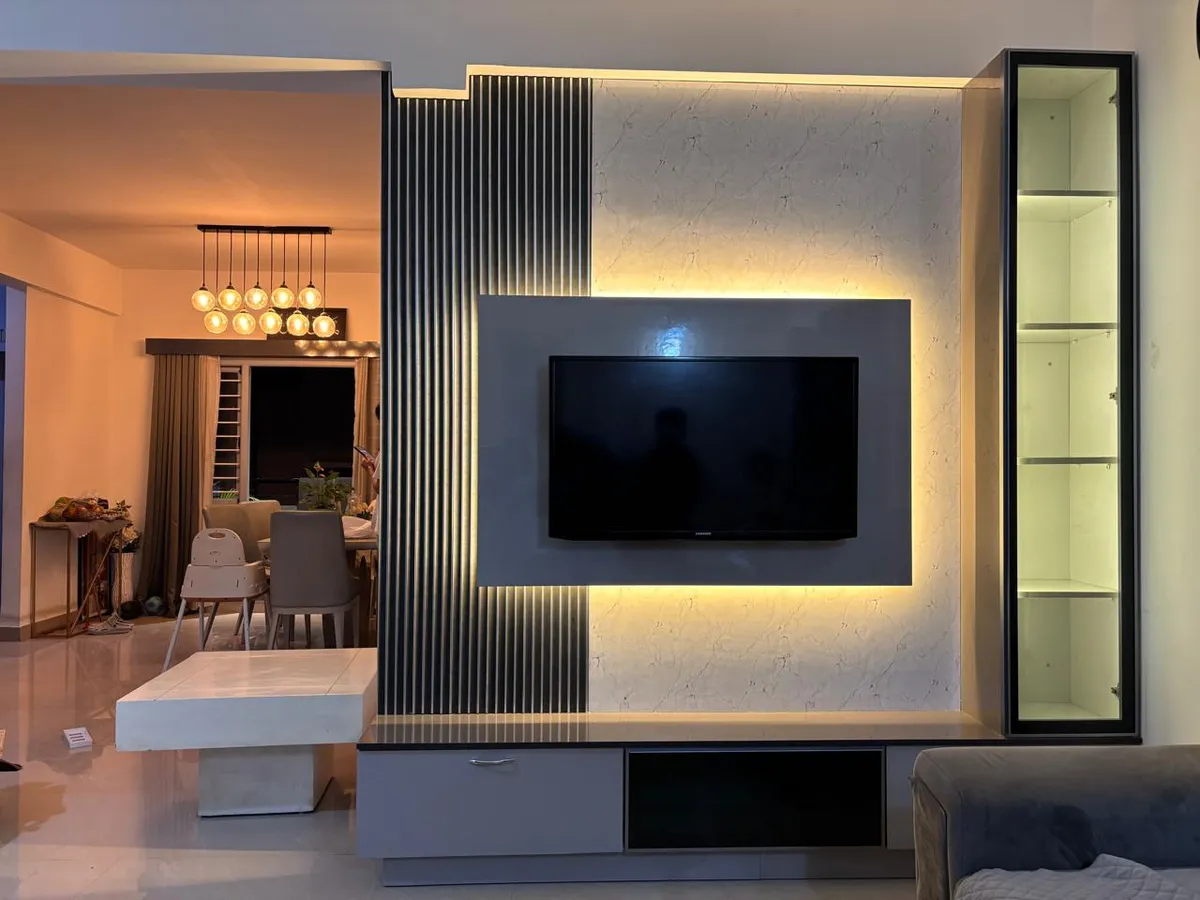 Evening shot of a grey TV wall combining a fluted vertical panel with a backlit marble-look field