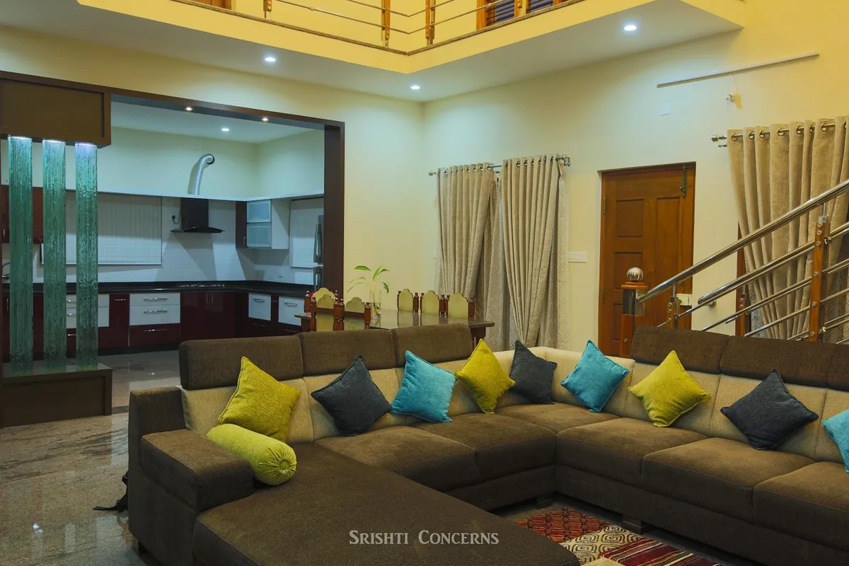 Double-height living room with an L-shaped brown sectional sofa styled with teal, olive and grey cushions, a glass water-feature column divider