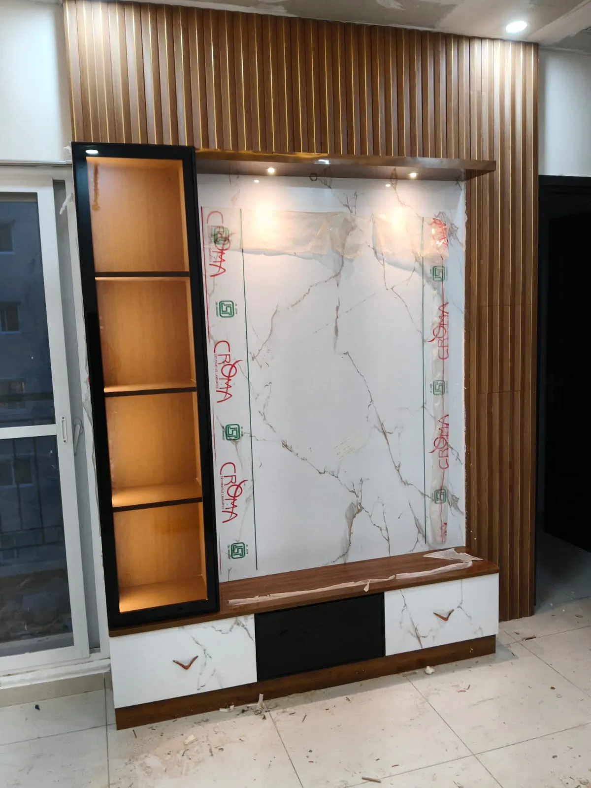 TV feature wall under installation with a wood-slat surround, a marble-clad panel still under protective film