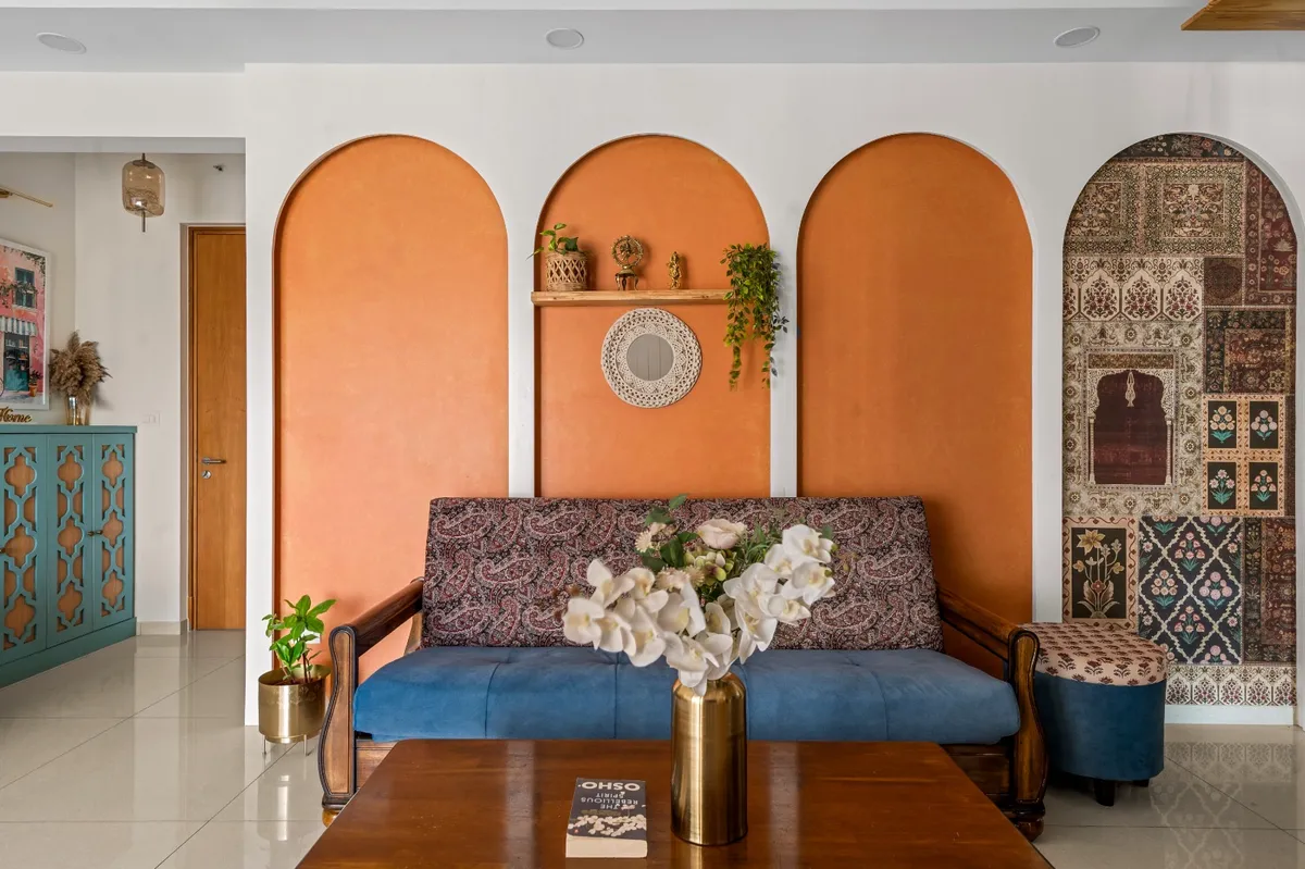 Living room where three terracotta arches are painted straight onto the white wall behind a wooden-armed sofa upholstered in blue and paisley