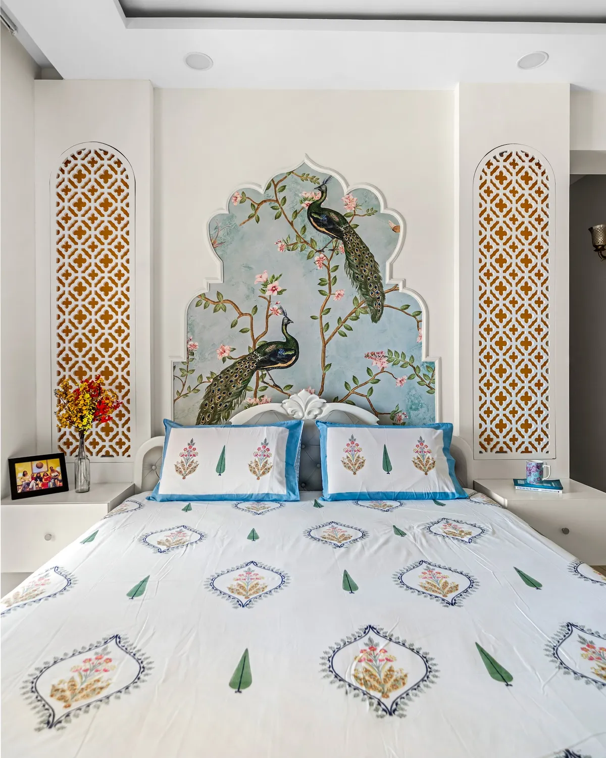 Bedroom with a peacock-and-blossom mural set inside a cusped Mughal arch behind a carved white headboard