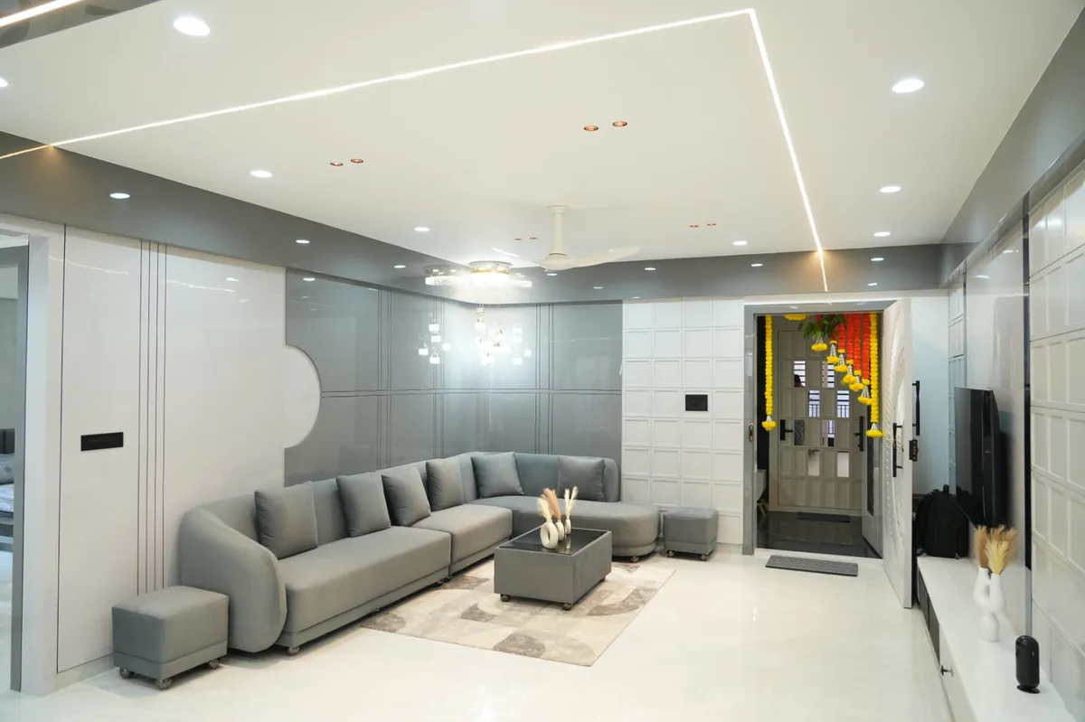 Grey high-gloss panelling with a curved cut-out behind a low L-sofa and wheeled ottomans, a mitred LED profile line tracing the white POP ceiling