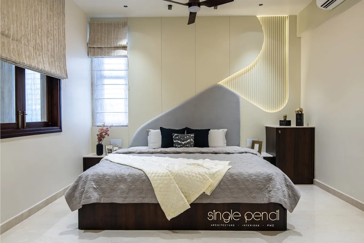 Bedroom where a curved grey velvet headboard sweeps up into a backlit fluted cream panel