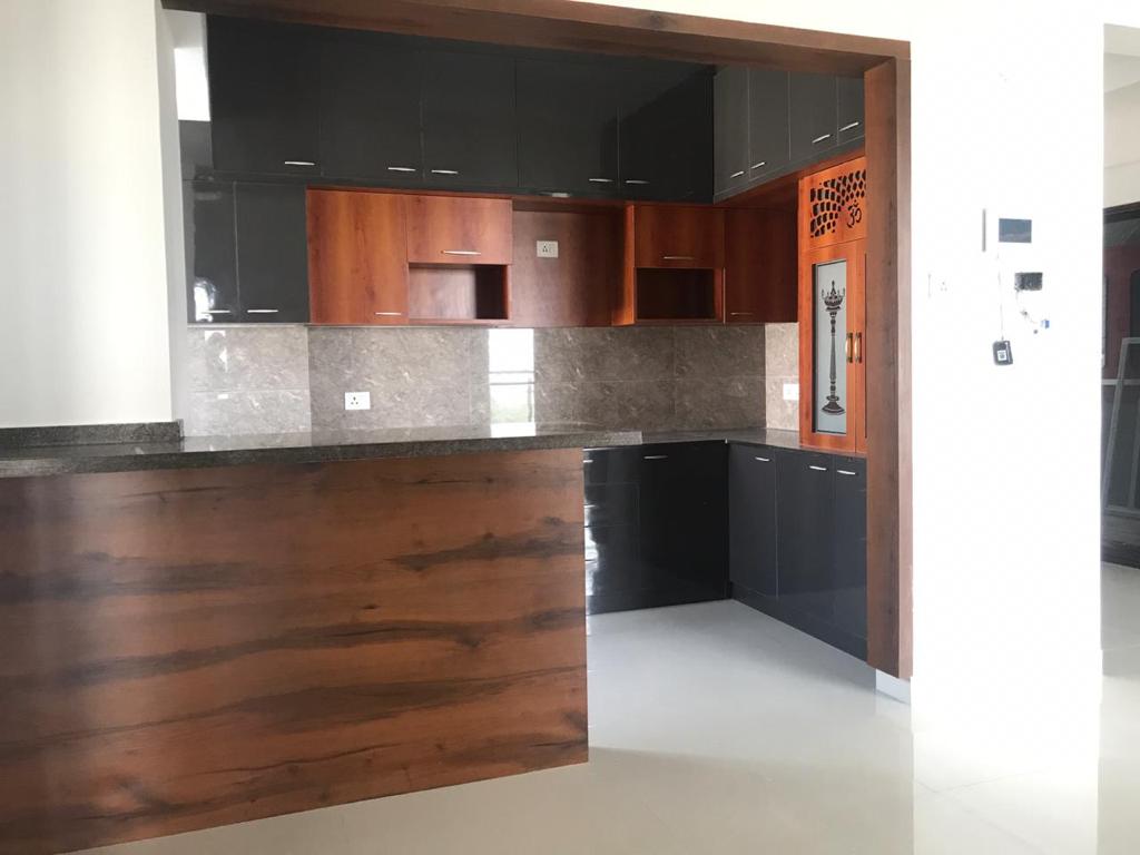L-shaped kitchen with glossy black cabinetry, wood-grain accent doors and a built-in jaali pooja unit in the corner