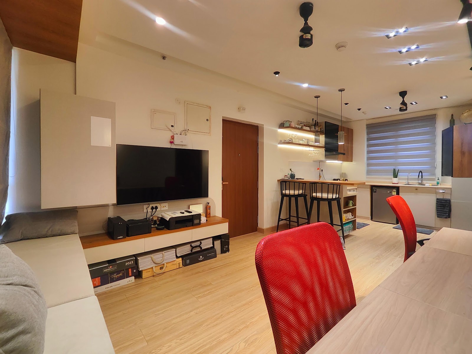 Open-plan studio apartment showing a wall-mounted TV unit and sofa in the living zone, a compact kitchen with breakfast counter