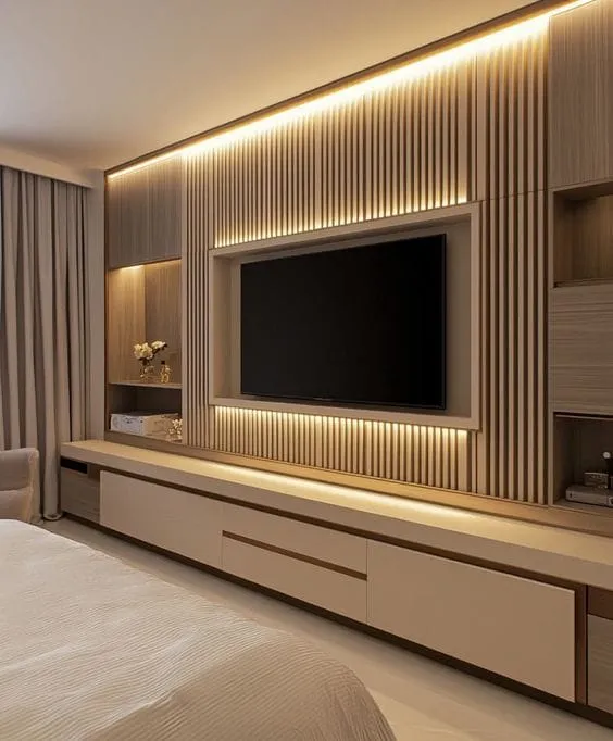 Bedroom TV feature wall with backlit vertical fluted wood panelling and a long floating storage console.