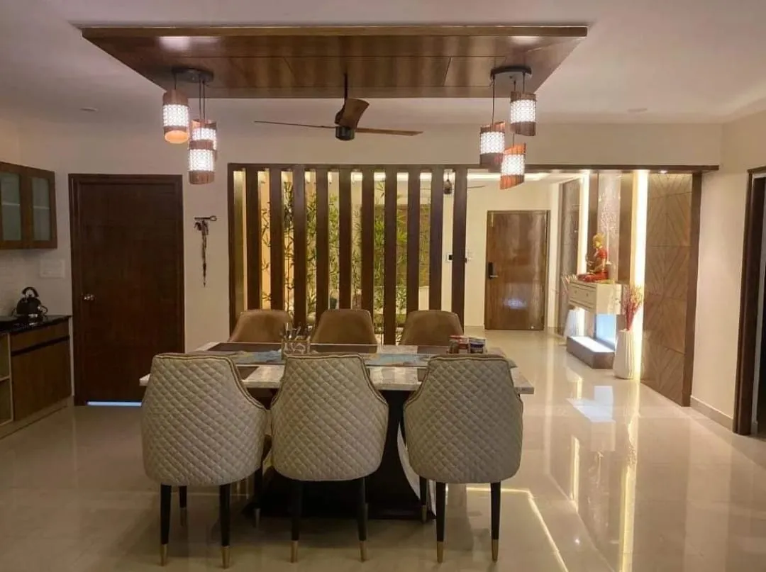 Six-seat marble-top dining table with quilted cream and tan chairs under a wood-clad ceiling raft and two clusters of cylindrical pendants