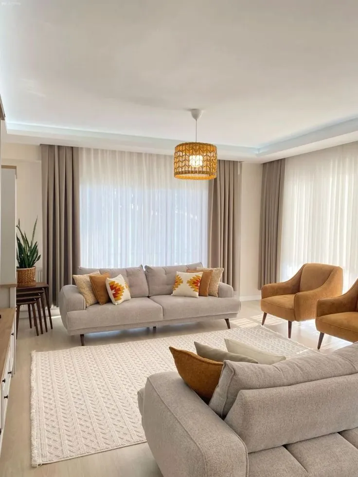Living room with two grey upholstered sofas dressed in mustard and cream cushions, a pair of mustard velvet armchairs, a rattan drum pendant light