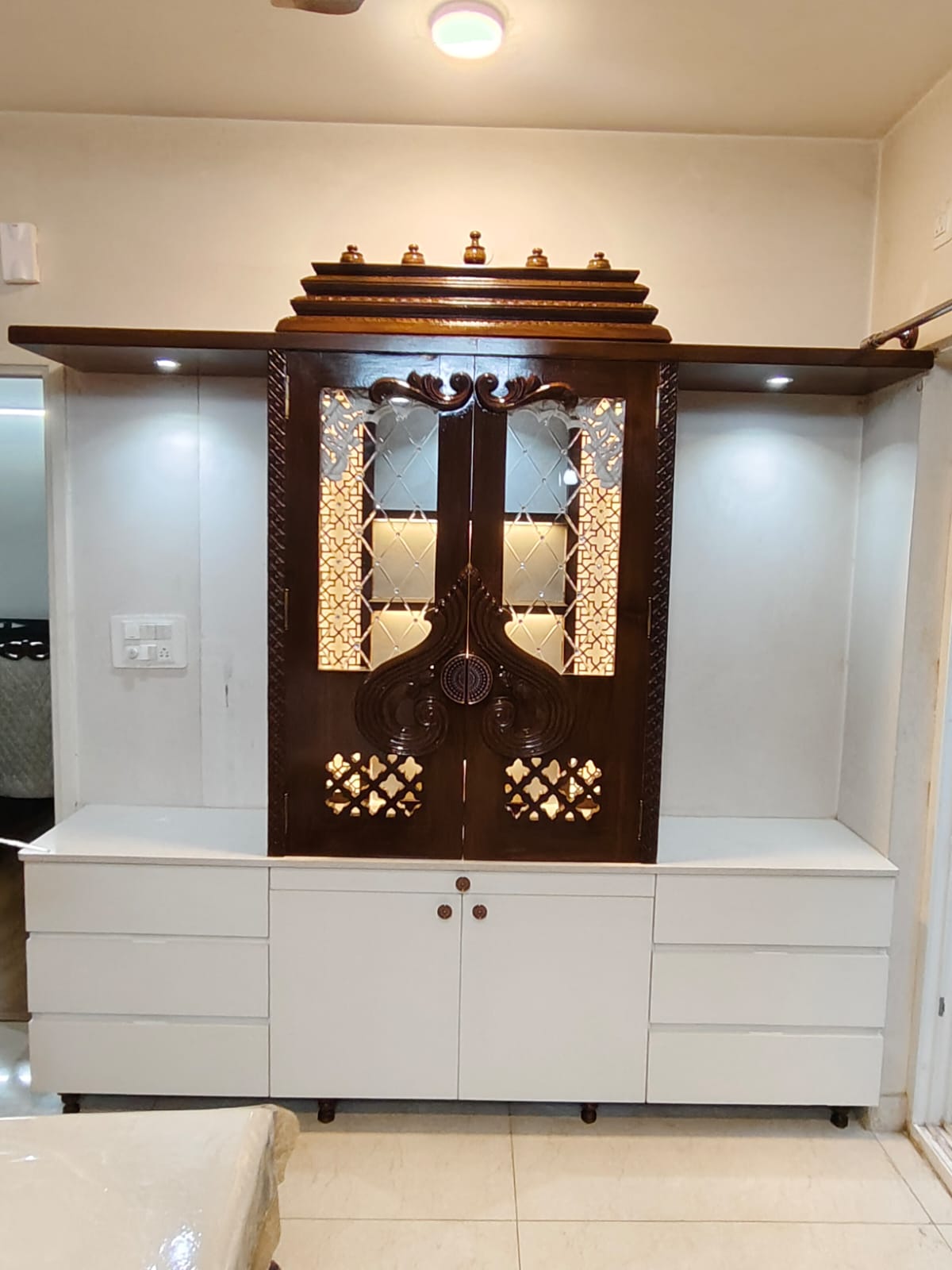 Built-in pooja unit with a carved dark-wood mandir cabinet featuring mirrored jaali-cut doors and backlighting