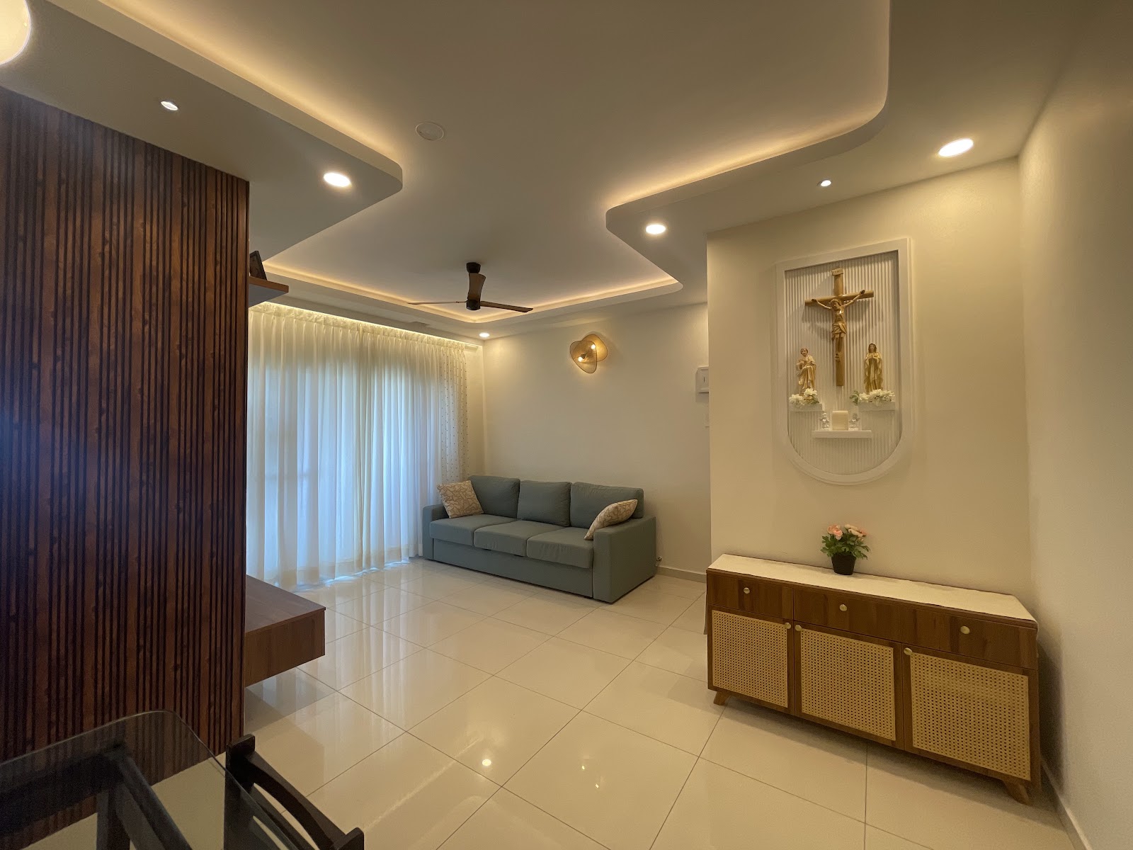 Living room with a stepped cove-lit false ceiling, a sage green sofa facing sheer curtains, a fluted wood partition wall