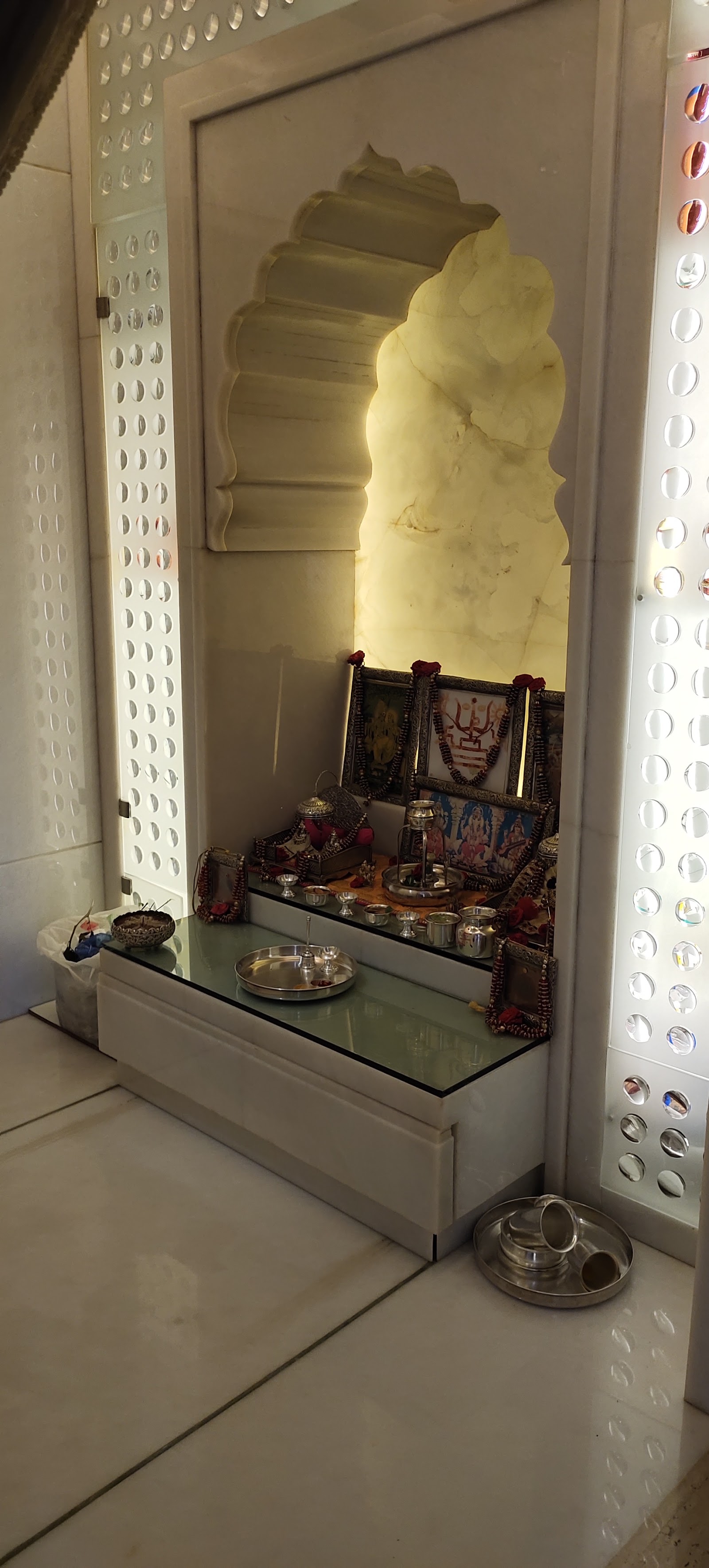 Backlit marble pooja unit with a Rajasthani-style arched onyx niche housing deity idols, flanked by perforated marble jaali panels