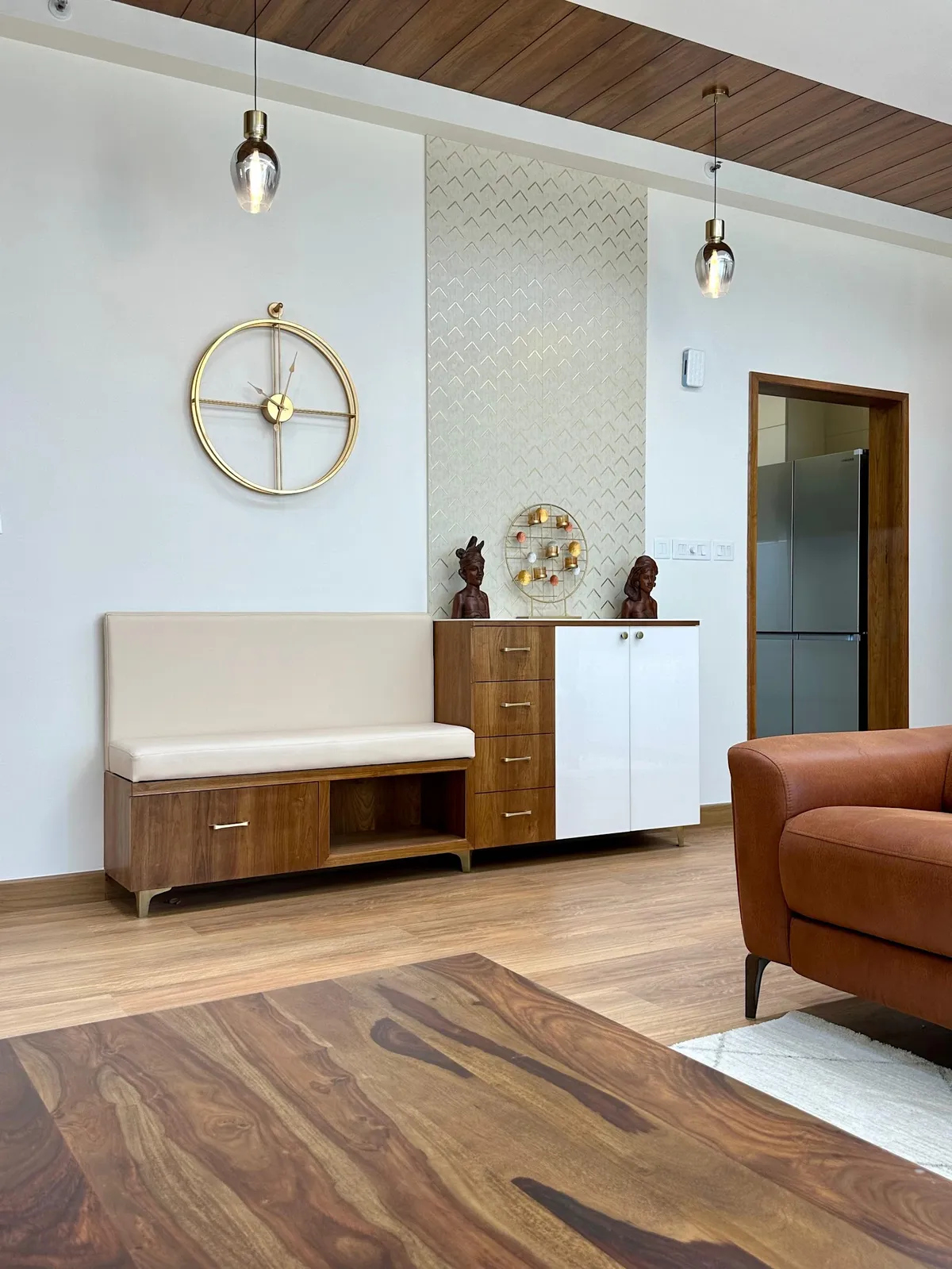 A dining nook with a built-in bench and walnut sideboard console below a herringbone-textured accent wall, brass pendant lights